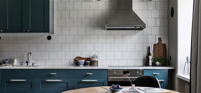 Køkken med hvide slagterfliser og mørkegrønne skabslåger. I køkkenet ser man også at der plads til et rundt spisebord