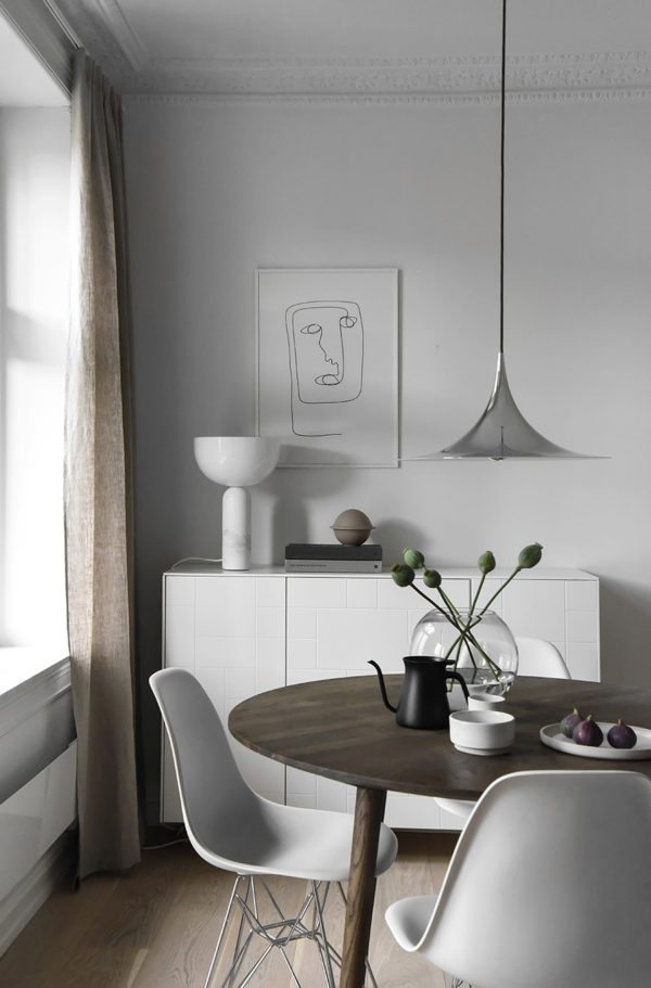 smuk og minimalistisk spisekrog med rundt mørkt træbord og en skænk i baggrunden med en flot lampe og en illustration indrammet på væggen