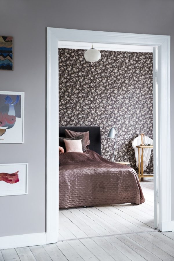 Et kig ind i et skønt soveværelse med brunblomstret tapet og seng med brunlig velour sengetæppe.