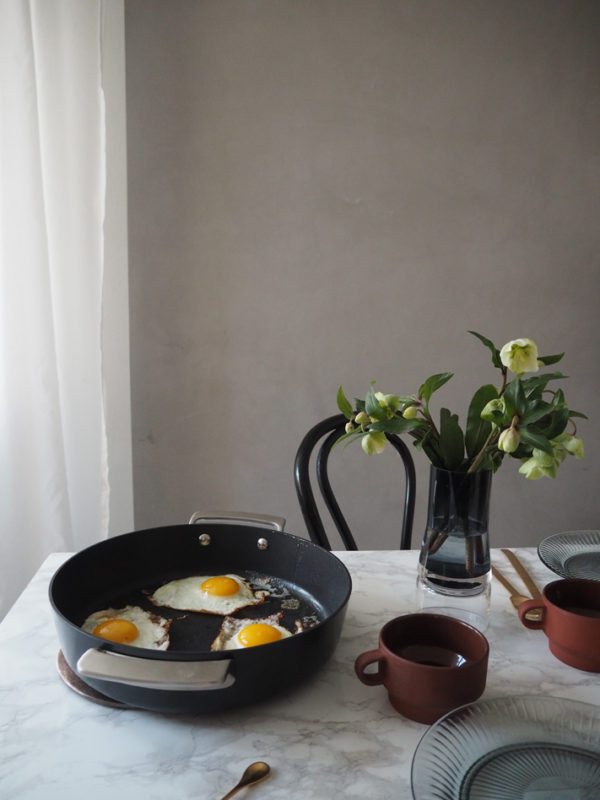 Morgenbord med spejlæg og kaffe placeret på flot marmor bord med franske cafestole omkring. 