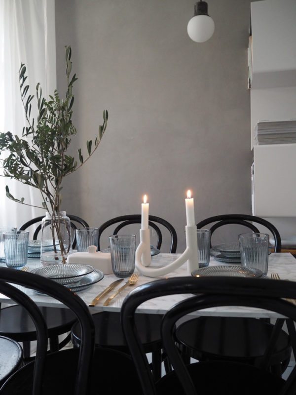 Bordedækning i stue med grå vægge. Bordet med marmorplade er dækket med blå glas og glastallerkner i Hammershøiserien fra Kähler Design. Levende lys og smukke olivengrene sætter en skøn stemning