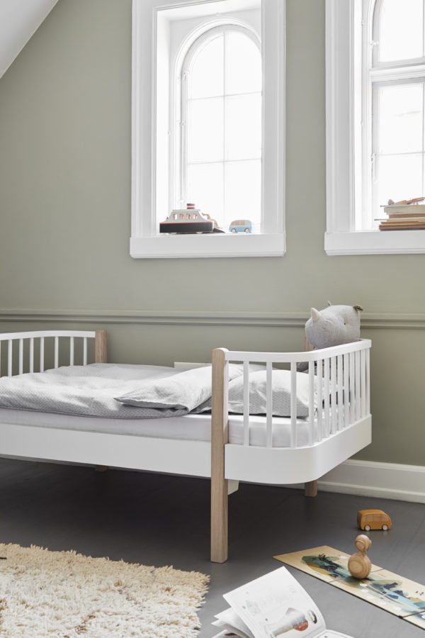 Smukt børnværelse med smuk skandinavisk seng i hvid og lys træ. Her er højt til loftet, smukke buede hvide vinduer og støvede grønne vægge