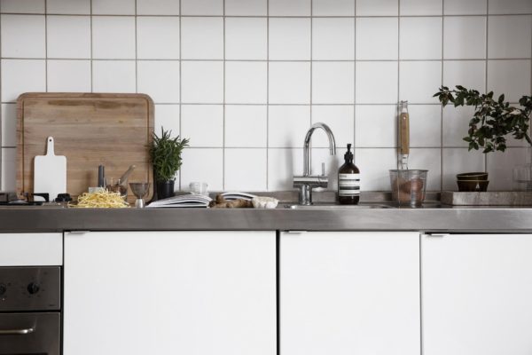 Her ses et køkken med hvide slagterfliser, hvide skabslåger og stål bordplade. Her er fuld gang i madlavningen